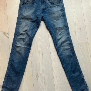 Replay Anbass jeans blå herr - Snygga blå Replay Anbass jeans med klassisk femficksdesign och diskret slitning. Jeansen har en smal passform och är tillverkade i mjukt denimtyg med stretch för extra komfort. Perfekta för dig som gillar en modern och stilren look.