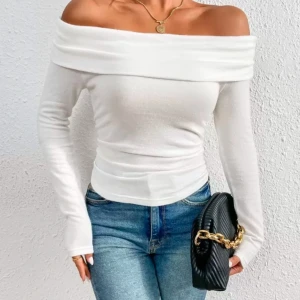Vit offshoulder långärmad topp - Snygg vit offshoulder topp med långa ärmar och bred krage som vilar över axlarna. Modellen är figurnära och har en stilren, enkel design. Materialet är mjukt och stretchigt, troligen bomull eller polyester. Perfekt att styla med jeans eller kjol för en trendig look.
