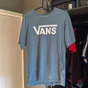 Blå Vans t-shirt med logga - Säljer en blå t-shirt från Vans med stor vit logga på bröstet. Klassisk rund hals och korta ärmar, perfekt för dig som gillar streetwear och enkel stil. Materialet är mjuk bomull som känns skönt mot huden. Passar dig som vill ha en chill och snygg look. Barn XL men lika stor som mina medium tröjor. 