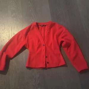 Röd fleecekofta från Zara - Riktigt snygg röd kofta från Zara i mjuk fleece. Koftan har v-ringning, markerad midja och knäppning med tre knappar framtill. Perfekt för lager-på-lager och ger en poppig färg till din outfit. Endast swish betalning skickas spårbart 59kr