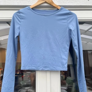 Ljusblå långärmad croppad topp - En stilren ljusblå långärmad topp med croppad passform. Toppen har rund halsringning och är tillverkad i ett mjukt, stretchigt material som känns skönt mot huden. Perfekt att matcha med jeans eller kjol för en enkel och fräsch look.