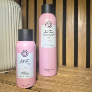 Shaping Heat Spray från Maria Nila - Två rosa flaskor med svart lock från Maria Nila, Shaping Heat Spray. Värmeskyddande spray som ger stadga och form till håret. Flaskorna är i olika storlekar och har en stilren design med vit etikett.