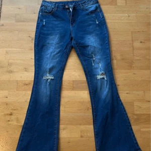 Blå bootcut jeans, S - Snygga blå bootcut jeans i storlek S med hål och detaljer på benen. Jeansen har klassisk femficksdesign och är tillverkade i en mix av bomull och polyester. Perfekta för dig som gillar en retroinspirerad look med extra vidd nedtill. Aldrig använda men prislapp osv finns ej kvar.