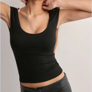 Svart croppad linnetopp med djup rygg - Säljer en svart, croppad linnetopp med djup rundad urringning både fram och bak. Toppen är ärmlös och har en tight passform som framhäver figuren. Perfekt att styla med höga byxor eller kjol för en trendig look.