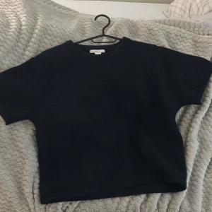 Svart t-shirt från Gina Tricot - En basic marinblå stickad tröja från Gina Tricot i storlek 158/164. Modellen är rak med korta ärmar och rund halsringning. Perfekt till jeans eller shorts för en enkel och clean look.