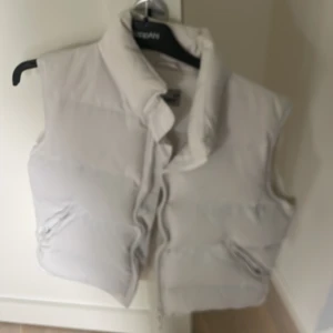 Vit dunväst från Athletic Sport - Snygg vit dunväst från Athletic Sport med hög krage och dragkedja framtill. Västen har två fickor med dragkedja och en stilren, enkel design som passar perfekt till lager-på-lager-stil. Perfekt för kyliga dagar när du vill hålla värmen utan att tumma på stilen.