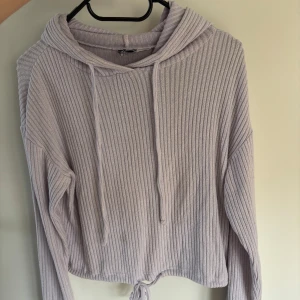 Ljuslila ribbad hoodie med snörning - Supermjuk ljuslila hoodie med ribbad struktur och snörning både i huvan och nertill. Tröjan har långa ärmar och en relaxed fit, perfekt för chill dagar. Snygg croppad modell som ger en trendig vibe.