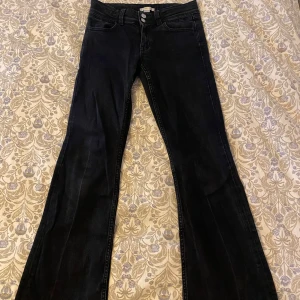 Svarta bootcut jeans med broderade fickor - Snygga svarta jeans med bootcut passform och klassisk femficksdesign. Jeansen har broderade bakfickor och stängs med dubbla knappar framtill. Perfekta för dig som gillar en tidlös look med lite extra vidd nertill.