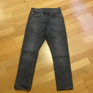 Levi's 501 svarta jeans straight fit - Klassiska svarta Levi's 501 jeans med rak passform. Jeansen har fem fickor, knappgylf och den ikoniska läderpatchen bak i midjan. Tillverkade i slitstarkt bomullsjeans med en mörk tvätt som ger en cool vibe.