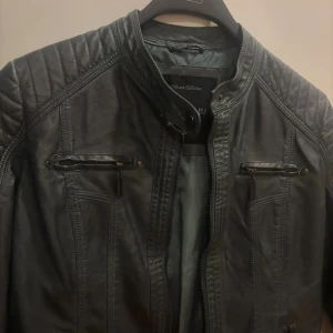 Skinnjacka storlek S - Snygg vintage svart skinnjacka från Dorohins med coola quiltade detaljer på axlarna och flera dragkedjefickor framtill. Jackan har en rak passform, ståkrage med tryckknapp och markerade sömmar som ger en edgy vibe.