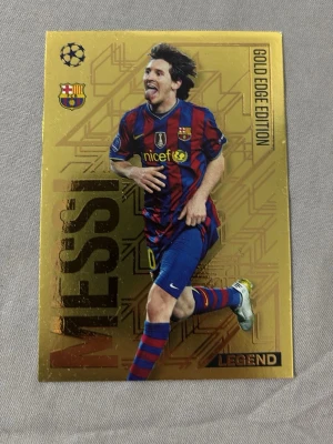 Messi Gold Edge Edition samlarkort - Exklusivt samlarkort från Topps Gold Edge Edition med Messi i FC Barcelonas klassiska rödblå matchställ. Kortet har guldfärgad bakgrund, klubbmärke och Champions League-logga. Perfekt för fotbollsfans och samlare som vill ha något unikt i sin kollektion. Köparen står för frakten.