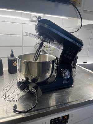 Svart köksassistent från Häws - Kraftfull köksassistent i svart plast och metall från Häws. Medföljer rostfri bunke, visp, degkrok och ballongvisp. Perfekt för bakning och matlagning, flera hastighetslägen och tydlig kontrollpanel på sidan.