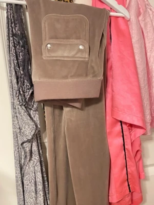 Beige velour loungewear-set - Mysigt beige loungewear-set i mjuk velour med ribbade muddar och fickor fram. Byxorna har dragsko i midjan och en liten broderad logga på ena fickan. Perfekt för chill dagar hemma eller när du vill vara bekväm men ändå se snygg ut.