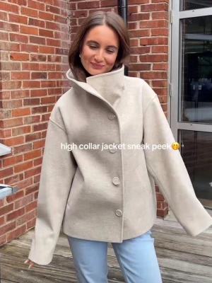 Beige jacka med hög krage och knappar - Stilren beige jacka med hög krage och stora knappar framtill. Jackan har en loose passform och är perfekt för lager-på-lager. Tillverkad i ett  mjukt material som ger en clean look. Passar snyggt till jeans eller dressade byxor.