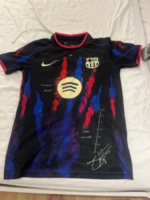 FC Barcelona x Nike matchtröja - Säljer en FC Barcelona matchtröja från Nike med unikt mönster i svart, blått och rött samt guldiga detaljer. Tröjan har klubbmärke, Nike-logga och Spotify-logga på bröstet samt tryck och signaturer. Perfekt för dig som älskar fotboll och vill sticka ut på planen.