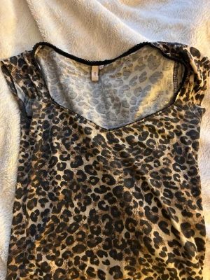 Leopardmönstrad topp med v-ringning - Snygg topp med leopardmönster och v-ringad hals. Toppen har korta ärmar och svarta spetsdetaljer längs halsringningen. Perfekt för dig som vill sticka ut lite extra.