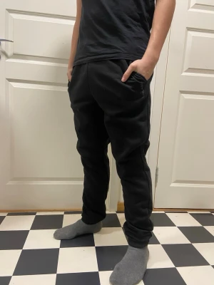 Svarta mjukisbyxor från Pilago  - Svarta mjukisbyxor från Pilago med elastisk midja och fickor på sidorna. Byxorna har en enkel och clean design med diskret logga på ena benet. Perfekta för chill dagar eller när du vill vara bekväm men ändå se snygg ut.