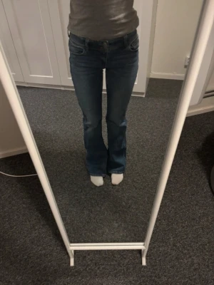 Blå bootcut jeans med fickdetaljer - Snygga blå bootcut jeans med klassiska fickor bak och fram. Jeansen har en lätt utsvängd passform nertill och låg midja. Perfekta för dig som gillar en tidlös och avslappnad stil. Passar till allt och är ett måste i garderoben.