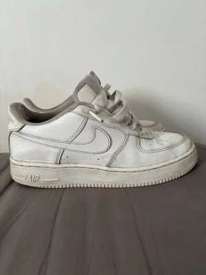 Vita Nike Air Force 1 sneakers - Klassiska vita Nike Air Force 1 sneakers med låg profil och rund tå. Skorna har snörning, perforerade detaljer på tån och är tillverkade i skinn med syntetdetaljer.
