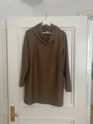 Brun stickad tröja med polokrage - Mysig brun stickad tröja med bred polokrage och långa ärmar. Tröjan har en avslappnad passform och diskreta ränder i materialet. Perfekt för kyliga dagar och enkel att matcha med jeans eller leggings.