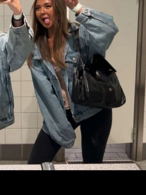 Oversized ljusblå jeansjacka - Säljer en oversized ljusblå jeansjacka med klassisk krage och knappar framtill. Jackan har två bröstfickor med lock och knapp samt sidfickor. Perfekt att slänga över en klänning eller till vardagslooken.