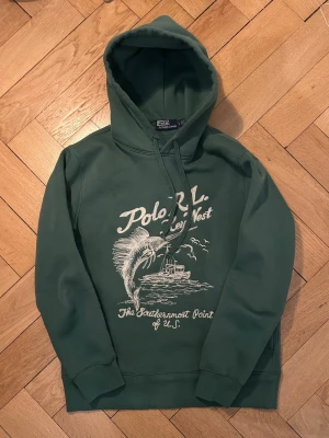 Polo Ralph Lauren hoodie - Mycket sällsynt mörkgrön key west hoodie från Polo Ralph Lauren med ett snyggt broderat motiv. Klassisk huva och ribbade muddar. Nyskick förutom två minimala fläckar (se bild 1). Lite ljusare färg i verkligheten. Nypris 3200. Tveka inte att höra av dig vid frågor eller funderingar!