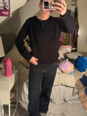 Svart stickad tröja i klassisk modell - En svart stickad tröja med rund hals och långa ärmar. Tröjan har en enkel, tidlös design med ribbade muddar vid ärmslut och nederkant. Perfekt att matcha med jeans eller kjol för en clean look. Storlek står inte men skulle säga S/M.