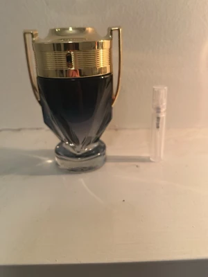 Paco Rabanne Invictus parfym - Snygg parfymflaska från Paco Rabanne i form av en pokal med gulddetaljer och mörkblå glas. Parfymen har en modern och sportig design som sticker ut på hyllan. Perfekt för dig som gillar exklusiva dofter och coola flaskor.