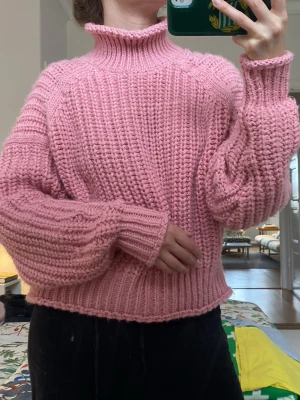 Rosa stickad polotröja - Mysig rosa stickad tröja med hög krage och breda, långa ärmar. Tröjan har en chunky ribbstickad struktur och avslutas med ribbade muddar vid ärmslut och nederkant. Perfekt för kalla dagar och ger en avslappnad men trendig look.