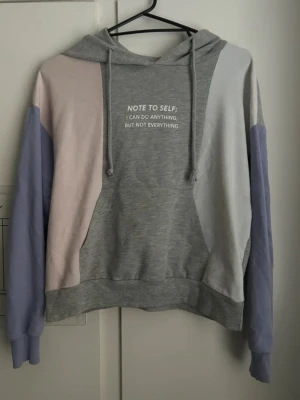 Grå hoodie - LCW - Färgglad hoodie med texten "NOTE TO SELF; I CAN DO ANYTHING, BUT NOT EVERYTHING" tryckt på framsidan. Den har en gråmelerad bas med färgblock i lila, rosa och vit på ärmarna och sidorna. Perfekt för en chill och trendig look.  Storlek: S Färg: Grå, lila, rosa och vit Märke: LCW Skick: Mycket 