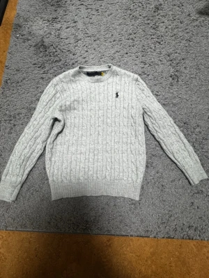 Grå polo Ralph lauren tröja  - Grå långärmad polotröja i storlek S. Tröjan har krympt något i tvätten och upplevs därför som något mindre i storleken, passar bäst XS eller en liten S. I övrigt i gott skick utan fläckar eller hål. En tidlös och lättmatchad bas i garderoben.