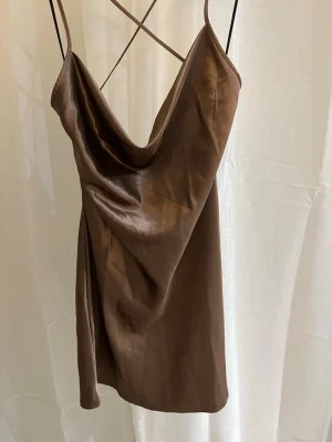 Brun satinklänning med tunna band - Brun satinklänning med tunna axelband och draperad uringning. Oanvänd med prislapp