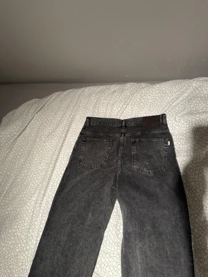 Mörkgrå jeans från Woodbird - Säljer ett par svarta jeans från Woodbird med klassisk femficksmodell och raka ben. Jeansen har bälteshällor och en diskret logga bak i midjan. Perfekta för dig som gillar en enkel och stilren look.