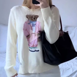 Ralph Lauren - Vit stickad tröja från Polo Ralph Lauren med ikoniska Polo Bear-motivet framtill. Björnen har rosa outfit, blå scarf och sneakers. Tröjan har rund halsringning, ribbade muddar och avslut. Köpt på Vinted för 1 år sedan 