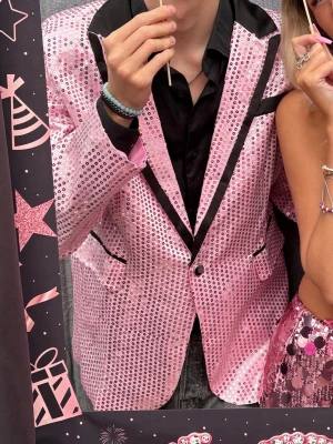 Rosa glittrig kavaj med paljetter - Säljer en rosa kavaj täckt med glittriga paljetter och svarta detaljer vid krage och fickor. Kavajen har en klassisk passform och stängs med en knapp framtill. Perfekt för dig som vill sticka ut på festen!