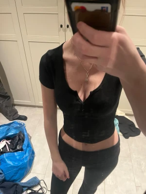 Svart croppad topp från Gina Tricot - Säljer en svart croppad topp från Gina Tricot med korta ärmar och v-ringning. Toppen har ribbad struktur och knappar framtill, vilket ger en snygg och trendig look. 