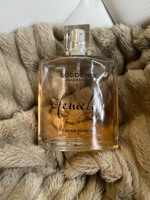 Suddenly Femelle Eau de Parfum - Fräsch parfym från Suddenly, modellen Femelle. Flaskan är rektangulär i genomskinligt glas med en stilren transparent kork. Doften är elegant och feminin, perfekt för dig som gillar klassiska och mjuka toner. Innehållet har en ljus bärnstensfärg.