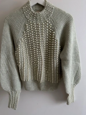 Ljusgrön stickad pärltröja från H&M-ny! - Supersnygg ljusgrön stickad tröja från H&M i alpackablandning. Tröjan har hög krage och är dekorerad med massor av vita pärlor framtill, på ärmarna och runt halsen. Ribbstickade muddar och en lyxig, trendig look som verkligen sticker ut.