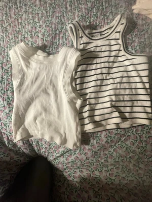 Två ribbade linnetoppar i vitt - Säljer två snygga linnetoppar från Gina tricot och Lindex i storleken 134/140. Ena toppen är helvit och ribbad, den andra är vit med svarta ränder och ribbad struktur. Båda är ärmlösa och har rund hals. Perfekta för varma dagar och kan enkelt matchas med jeans eller shorts. Har haft länge men i inte dåligt skick. Tvättat många gånger! En snygg duo. 50 kr för båda!!