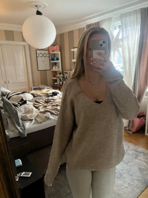 Beige stickad tröja med v-ringning - Mysig beige stickad tröja med djup v-ringning och långa ärmar. Tröjan har en avslappnad passform och är perfekt för lager-på-lager. Passar till både jeans och leggings för en chill look.