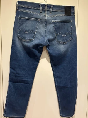 Replay Anbass jeans - Snygga blå jeans från Replay med klassisk femficksdesign. Jeansen har diskreta slitningar framtill och ljusare partier för en cool look. Tillverkade i mjukt denimtyg med detaljerade sömmar på bakfickorna.