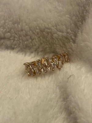 Guldfärgad ring ✨ elegant med gnistrande stenar - Stilren guldfärgad ring dekorerad med små rektangulära stenar som ger ett elegant och lyxigt uttryck ✨ Perfekt om du vill ha något som glittrar lagom mycket – funkar både till vardag och fest. ✨ Elegant & feminin ✨ Gnistrande stenar i rad ✨ Lätt att matcha med andra smycken I mycket fint skick 🤍 Skickas snabbt 📦 Skriv gärna om du vill ha fler bilder eller har frågor!