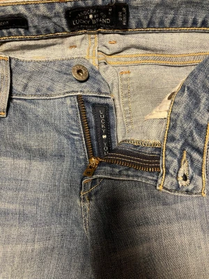 Blå bootcut jeans från Lucky Brand - Lågmidjade ljusblå bootcut jeans från Lucky Brand med klassisk femficksdesign, dragkedja och knappstängning. Jeansen har råa, fransiga benslut och är tillverkade i mjukt denimtyg som ger en avslappnad vibe. Passar mig som är 160cm. 🌸💞