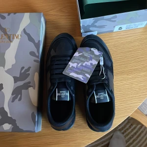 Valentino Garavani svarta sneakers - Svarta sneakers från Valentino Garavani med coola camouflagemönster i grå och beige toner. Snygg, chunky sula med mönster undertill och klassisk snörning. Märkeslogga på plösen och detaljer i skinn. Kommer med extra svarta skosnören och dustbag. Hör av er vid frågor 