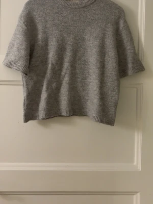 Grå stickad t-shirt - En enkel och stilren grå stickad t-shirt med korta ärmar och rund hals. Tröjan har en rak passform och ribbstickade kanter vid ärmslut, hals och nederkant. Perfekt för lager-på-lager och passar till många olika outfits. Bara att fråga ifall du undrar något eller vill ha fler bilder! Pris kan diskuteras💞