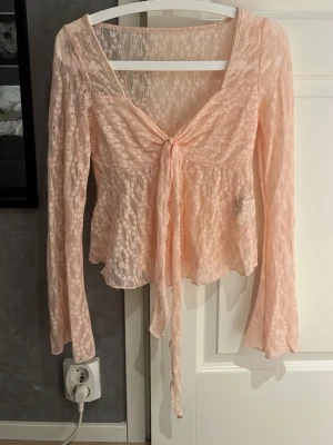 Ljusrosa spetsblus med knyt - Söt ljusrosa topp i genomskinlig spets med långa ärmar och knyt framtill. Djup v-ringning och lätt utsvängd nederkant ger en romantisk vibe. Perfekt för lager på lager och trendiga outfits. helt ny. säljer pågrund av att jag inte passa.😇😇