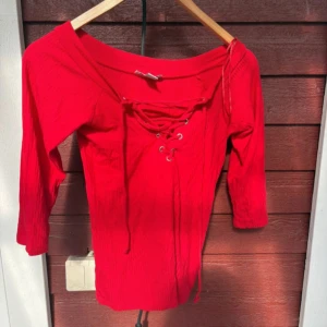 Röd ribbad topp med snörning från Amisu - Säljer en snygg röd ribbad topp från Amisu i storlek S. Toppen har snörning framtill och en bred halsringning. Ärmarna är trekvarts och materialet känns mjukt och stretchigt. Perfekt för dig som gillar färg och coola detaljer!