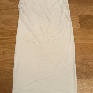 Vit axelbandslös kortklänning - Säljer en enkel vit axelbandslös kortklänning med rak passform. Klänningen är gjord i mjukt bomullsmaterial och har en clean look utan mönster eller detaljer. Perfekt för dig som gillar minimalistisk stil.