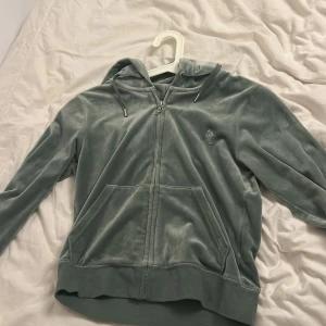 Grön hoodie och byxor från Juicy Couture - Mjuk och chill grön hoodie från Juicy Couture i velour med dragkedja, huva och snörning. Långärmad med känguruficka framtill och broderad logga på bröstet. Perfekt för dig som gillar comfy vibes och snygg streetstyle. Storlek m i tröja storlek S i byxor 