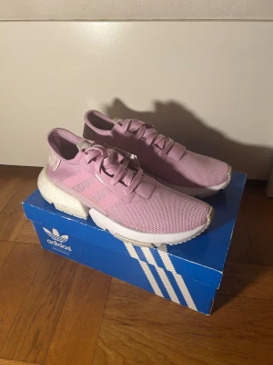 Adidas lila sneakers - Säljer ett par Adidas  sneakers i ljusrosa med klassiska tre ränder på sidan. Skorna har en stickad ovandel i syntetmaterial, snörning och en vit boost-sula som ger grym komfort. Perfekt för dig som gillar sportig och clean stil.